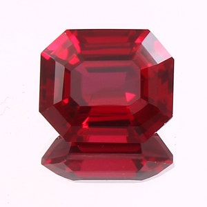 May include: A deep red gemstone with a square emerald cut. The gemstone is faceted and has a high polish.