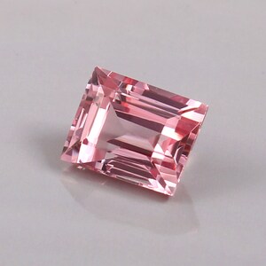 May include: A pink, rectangular, faceted gemstone with a step cut.