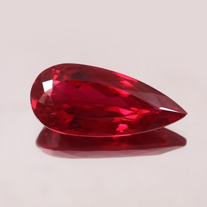 Puede incluir: Una piedra preciosa de rubí en forma de pera con un color rojo intenso. La piedra preciosa está facetada y tiene un alto pulido.