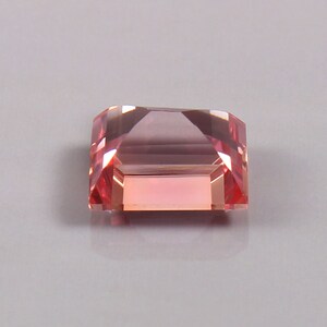 May include: A pink and peach coloured gemstone with a rectangular shape and a faceted cut.