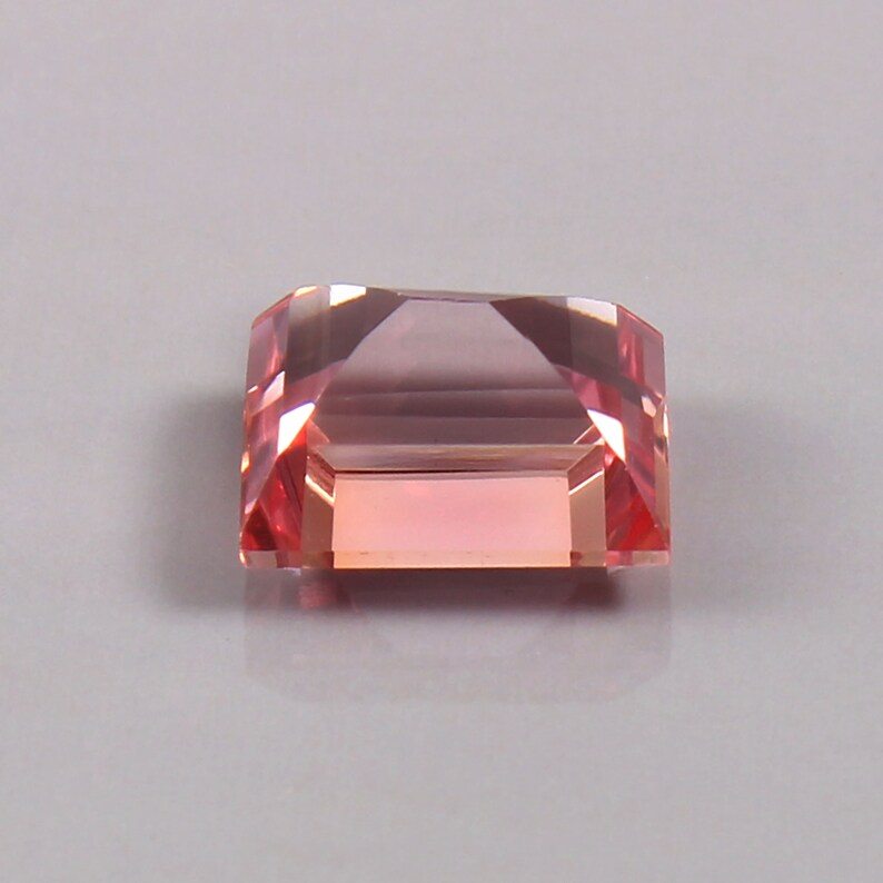 May include: A pink and peach coloured gemstone with a rectangular shape and a faceted cut.