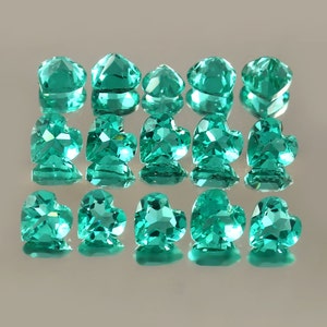 Puede incluir: Una colección de 15 piedras preciosas de color verde azulado en forma de corazón. Las piedras preciosas están dispuestas en tres filas de cinco, con cada fila ligeramente desplazada de la que está arriba.