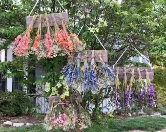 May include: Four rectangular wooden planks suspended by white ropes, each featuring multiple bundles of dried flowers tied with twine. The floral arrangements display a variety of colors including pink, orange, blue, purple, and white baby's breath.