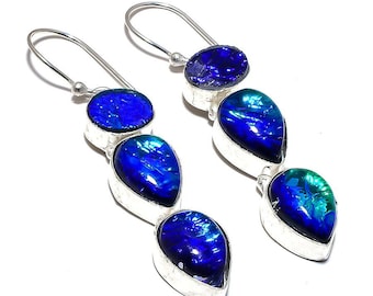 May include: Silver-tone dangle earrings with three blue, teardrop-shaped stones. The stones have a shimmering, iridescent quality, with hints of green and blue. The earrings have a hook closure.
