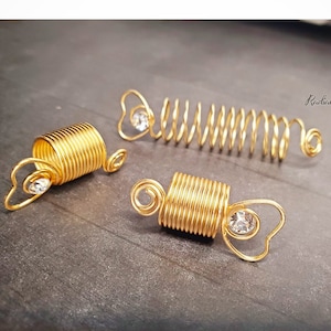 Puede incluir: Tres espirales para el cabello doradas con un acento de corazón de cristal transparente. Las espirales están hechas de alambre y están diseñadas para ser usadas como extensiones de cabello.