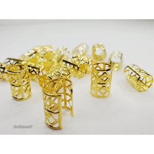 May include: A group of gold-colored metal hair cuffs with a geometric design. The cuffs are scattered on a white surface.