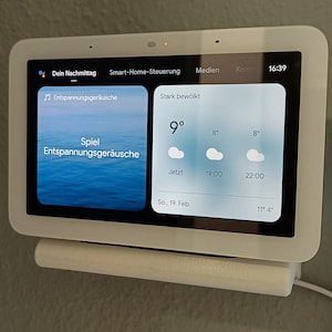 Puede incluir: Un dispositivo blanco de domótica con una pantalla táctil que muestra el pronóstico del tiempo actual y un reproductor de música. La pantalla muestra el texto "Stark bewölkt" (fuertemente nublado) y una temperatura de 9 grados Celsius. La hora es 16:39.