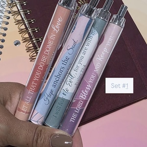 May include: A set of four clear pens with inspirational quotes in various colors. The pens have silver accents and are displayed on a notebook. The quotes include "Let all that you do be done in Love," "Hope anchors the Soul," "I will fear No Evil, for you are with me," and "The Lord Bless You and Keep You."