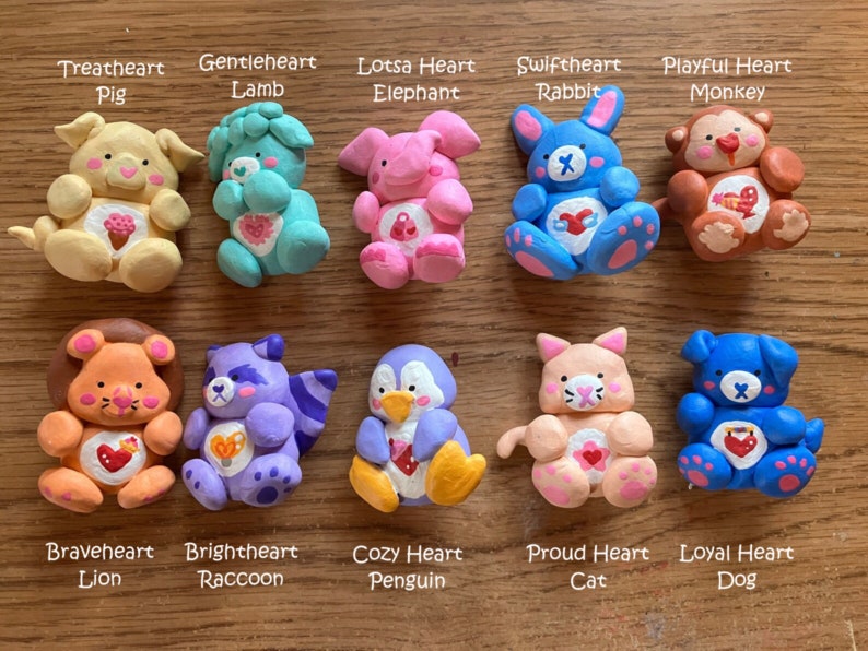 May include: Ten handmade clay figurines of various animals, each with a heart and a name. The animals include a pig, lamb, elephant, rabbit, monkey, lion, raccoon, penguin, cat, and dog. Each figurine is painted in bright colors and has a unique design.