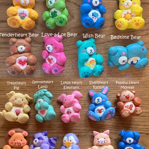 May include: A collection of handmade Care Bear figurines, each with a unique design and color scheme. The figurines are made of clay and feature various animal characters, including a pig, lamb, elephant, rabbit, and monkey. The figurines are all wearing the iconic Care Bear logo and have a heart on their chest.