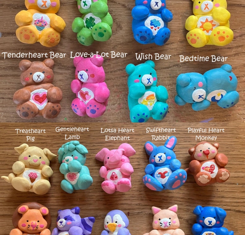 May include: A collection of handmade Care Bear figurines, each with a unique design and color scheme. The figurines are made of clay and feature various animal characters, including a pig, lamb, elephant, rabbit, and monkey. The figurines are all wearing the iconic Care Bear logo and have a heart on their chest.