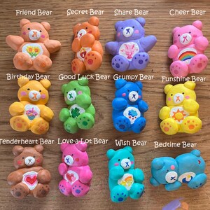 May include: Twelve colorful Care Bear figurines with different designs and names. Each bear has a unique color and symbol on its chest. The bears are arranged in three rows of four.