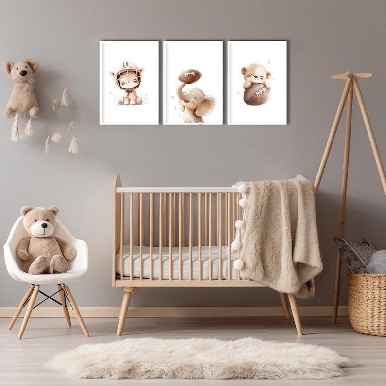 May include: Three framed illustrations of animals playing football. The illustrations are in a watercolor style and feature a brown bear, an elephant, and a deer. The illustrations are hung on a light gray wall above a wooden crib.