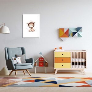 May include: A watercolor illustration of a cute giraffe wearing a helmet, printed on a white background and framed in a white frame. The print is hanging on a white wall in a nursery room with a crib, a chair, and a small table with toys.