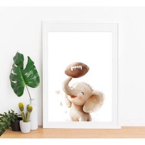 May include: A white framed print featuring a cartoon illustration of a smiling elephant holding a brown football above its head.