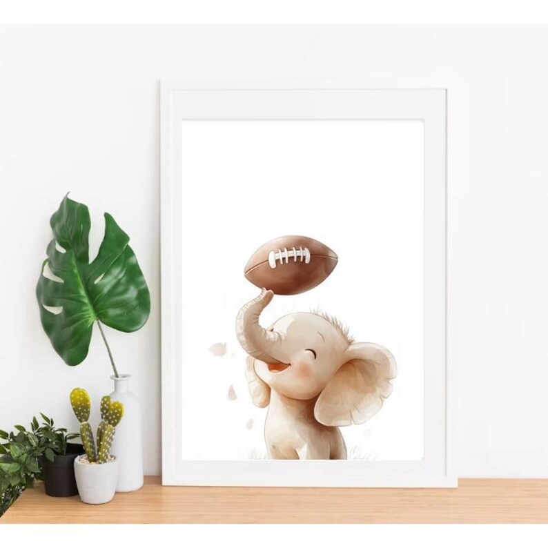 May include: A white framed print featuring a cartoon illustration of a smiling elephant holding a brown football above its head.