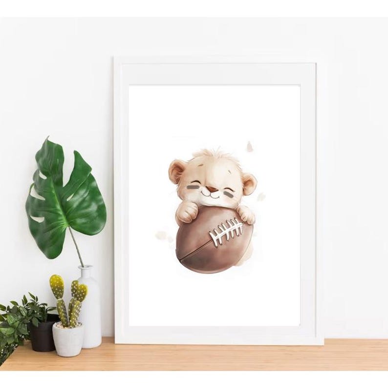 May include: A white framed print featuring a cute cartoon lion cub holding a brown and white football. The lion cub is smiling and has a light brown coat.