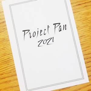 Puede incluir: Una hoja de papel blanca con un borde negro y el texto "Project Pan 2021" escrito en cursiva negra.