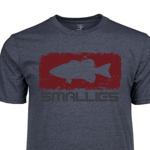 May include: Navy blue t-shirt with a distressed red rectangle containing a fish silhouette. The word "SMALLIES" is printed in gray below the rectangle. The shirt has short sleeves and a crew neck.