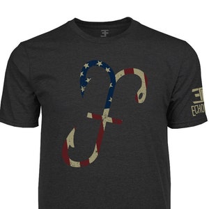 Puede incluir: Camiseta gris oscuro con una letra "F" estilizada en forma de anzuelo, con un diseño de bandera estadounidense desgastada. La camiseta tiene cuello redondo y mangas cortas. El texto "3F ECHO" está impreso en la manga derecha.