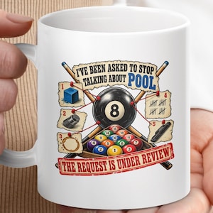 May include: A white ceramic mug featuring a graphic illustration of pool equipment, including an 8-ball, a rack of billiard balls, and cues. The text reads I'VE BEEN ASKED TO STOP TALKING ABOUT POOL and THE REQUEST IS UNDER REVIEW with numbered diagrams.