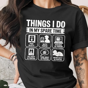 May include: Black t-shirt with white text and graphics. The text reads "THINGS I DO IN MY SPARE TIME" with illustrations of 3D printing activities: printing objects, watching a printer, researching, talking about, thinking about, and dreaming about 3D printing.