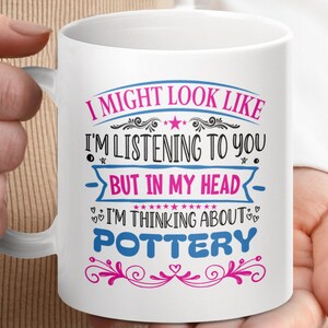 May include: White ceramic mug with a pink and blue design. The mug features the text "I might look like I'm listening to you, but in my head I'm thinking about pottery."
