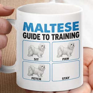 Puede incluir: Taza de cerámica blanca con el texto "MALTESE GUIDE TO TRAINING" en azul. La taza muestra un perro maltés demostrando los comandos: Sit, Paw, Fetch y Stay. La taza está sujeta por una persona.