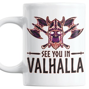 Puede incluir: Taza de cer&aacute;mica blanca con una ilustraci&oacute;n en negro y morado de una calavera con un casco con cuernos y hachas cruzadas. El texto "See you in Valhalla" est&aacute; impreso debajo de la ilustraci&oacute;n.