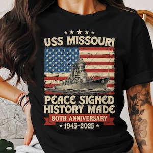 May include: Black t-shirt featuring a distressed American flag design with the USS Missouri battleship. Text includes "USS Missouri," "Peace Signed History Made," and "80th Anniversary 1945-2025."