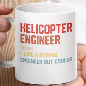 May include: White ceramic mug with a red, orange and blue design. The text on the mug reads "Helicopter Engineer (noun) I. Like a normal engineer but cooler."