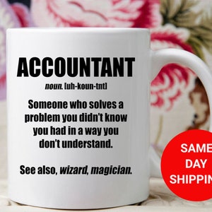 May include: White ceramic coffee mug with a black graphic that reads "ACCOUNTANT noun. luh-koun-tntl Someone who solves a problem you didn't know you had in a way you don't understand. See also, wizard, magician."
