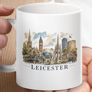 May include: White ceramic mug with a watercolour illustration of Leicester, England. The design includes iconic buildings, a clock tower, and the city's name. A great gift for anyone who loves Leicester.