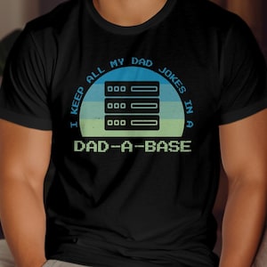 May include: A black t-shirt featuring a retro-style graphic of a server database. The text reads "I keep all my dad jokes in a dad-a-base".
