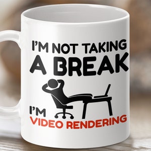 May include: White ceramic mug with black text that reads "I'm not taking a break I'm video rendering". A black silhouette of a person sitting in a chair with a laptop is above the text.
