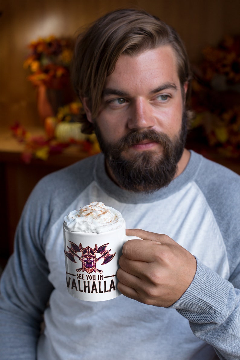 Puede incluir: Una taza de cer&aacute;mica blanca con un gr&aacute;fico negro y morado de una calavera con hachas cruzadas. La taza tiene el texto "See you in Valhalla" impreso en ella. La taza est&aacute; llena de una bebida cremosa cubierta con canela.