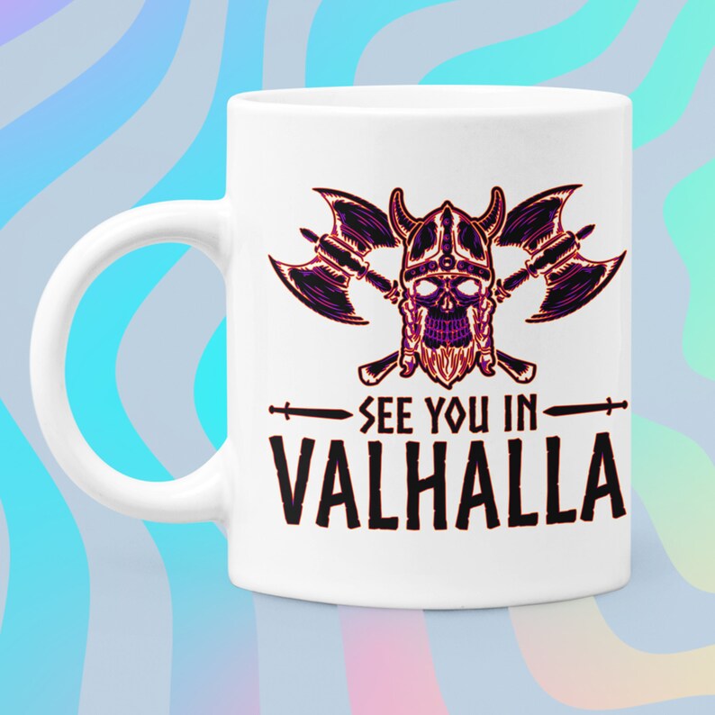 Puede incluir: Taza de cer&aacute;mica blanca con una ilustraci&oacute;n en negro y morado de una calavera vikinga con hachas cruzadas y el texto "See you in Valhalla".