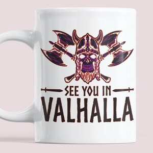 Puede incluir: Taza de cer&aacute;mica blanca con una ilustraci&oacute;n en negro y morado de una calavera vikinga con hachas cruzadas y el texto "See you in Valhalla".
