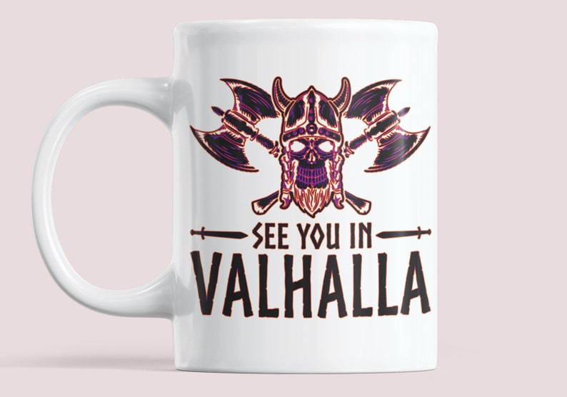 Puede incluir: Taza de cer&aacute;mica blanca con una ilustraci&oacute;n en negro y morado de una calavera vikinga con hachas cruzadas y el texto "See you in Valhalla".