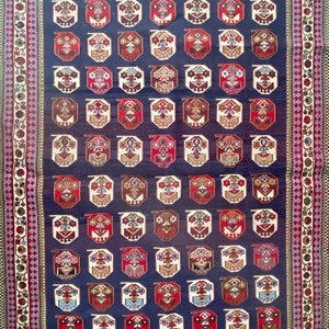 Op de afbeelding: Een traditioneel Turks tapijt met een donkerblauwe achtergrond en ingewikkelde geometrische patronen in tinten rood, wit en bruin. Het tapijt heeft een rand met bloemmotieven.