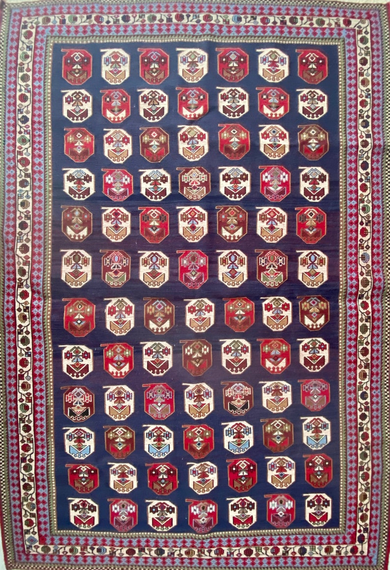 Op de afbeelding: Een traditioneel Turks tapijt met een donkerblauwe achtergrond en ingewikkelde geometrische patronen in tinten rood, wit en bruin. Het tapijt heeft een rand met bloemmotieven.