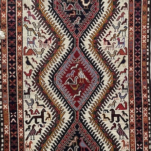 May include: A traditional rug with a white background and a central diamond pattern. The diamond is filled with a variety of colors, including red, blue, and green. The rug is surrounded by a border of geometric designs.