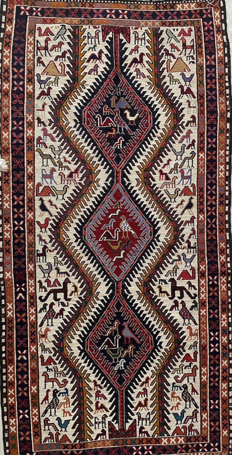 May include: A traditional rug with a white background and a central diamond pattern. The diamond is filled with a variety of colors, including red, blue, and green. The rug is surrounded by a border of geometric designs.