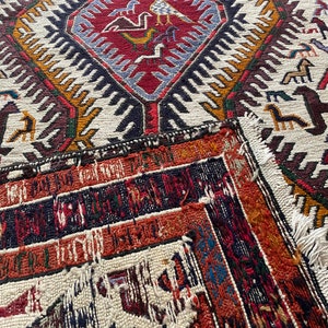 May include: A vintage rug with a geometric pattern in shades of red, blue, white, and black. The rug has a frayed edge and is made of wool.