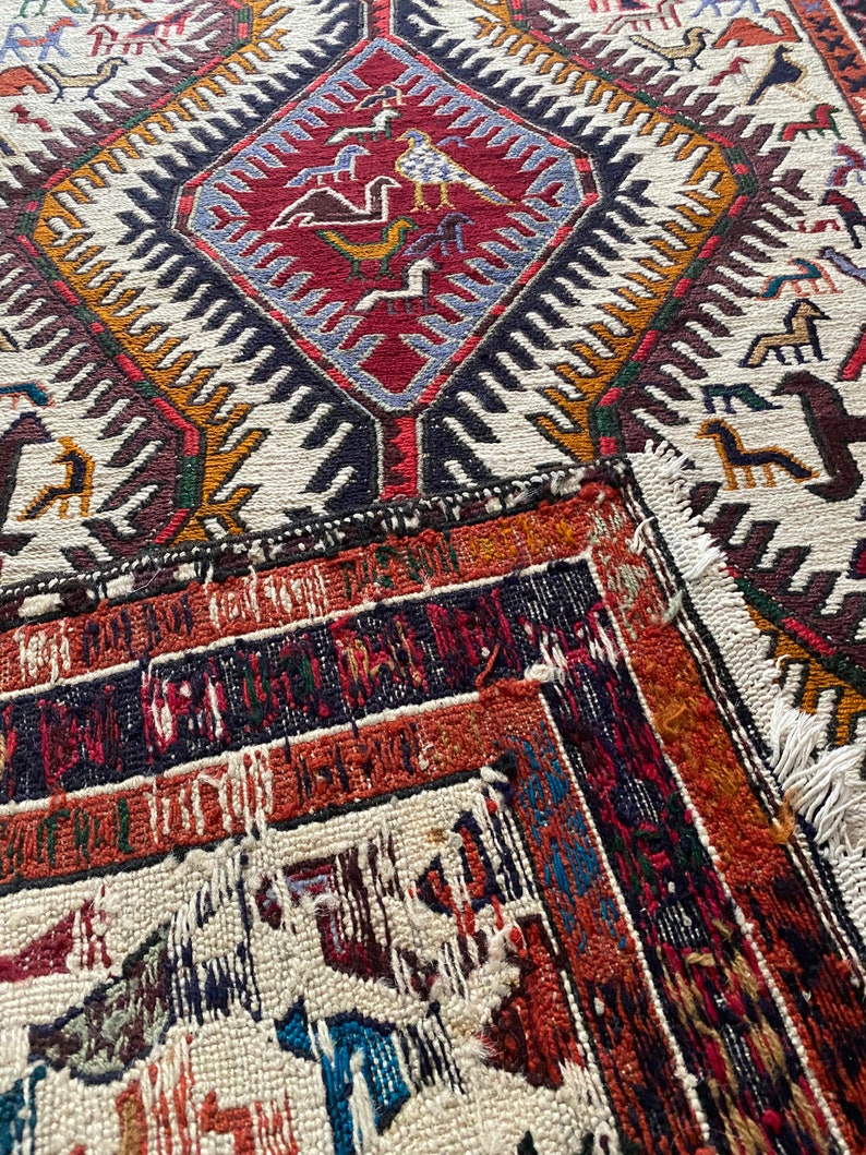 May include: A vintage rug with a geometric pattern in shades of red, blue, white, and black. The rug has a frayed edge and is made of wool.