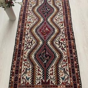 May include: A traditional rug with a cream background and a geometric pattern in shades of red, orange, blue, and black. The pattern features stylized birds and animals.