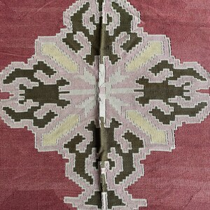 May include: A close-up of a red fabric with a white and brown geometric pattern. The pattern is symmetrical and features a diamond shape in the center.