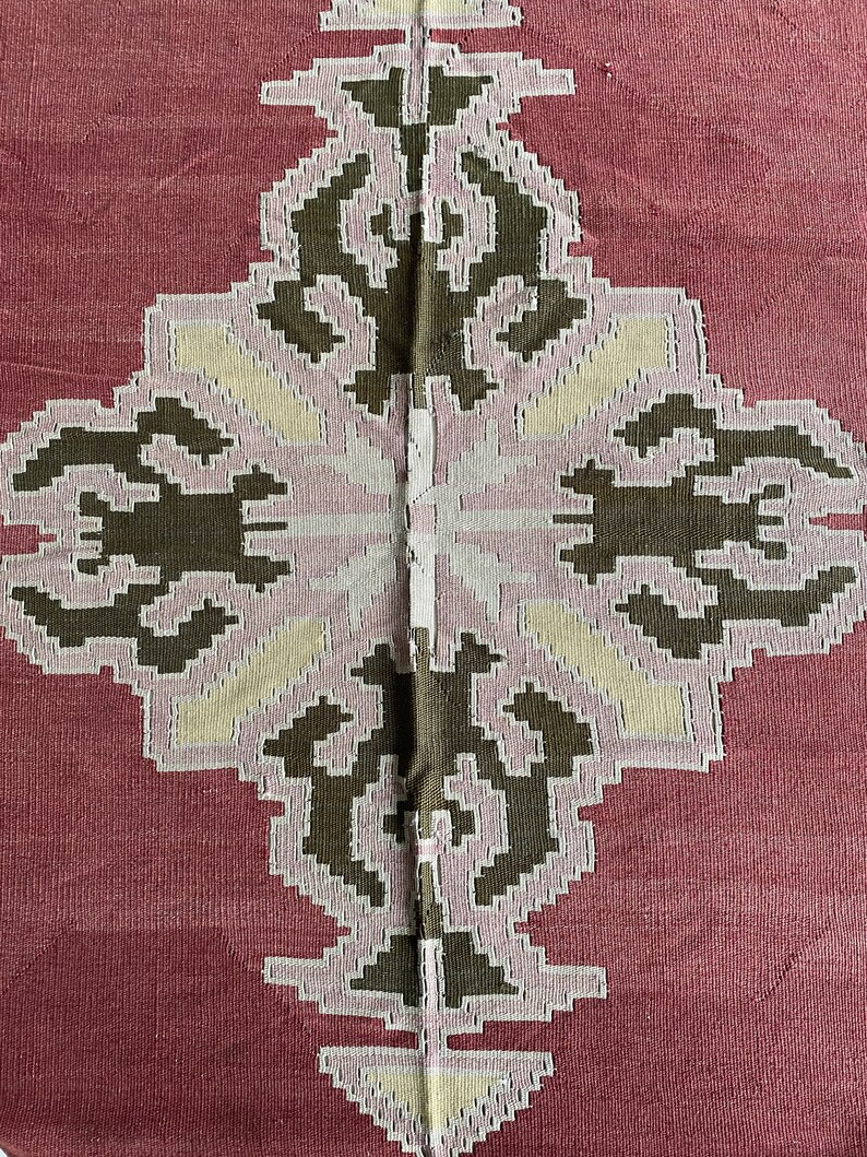May include: A close-up of a red fabric with a white and brown geometric pattern. The pattern is symmetrical and features a diamond shape in the center.