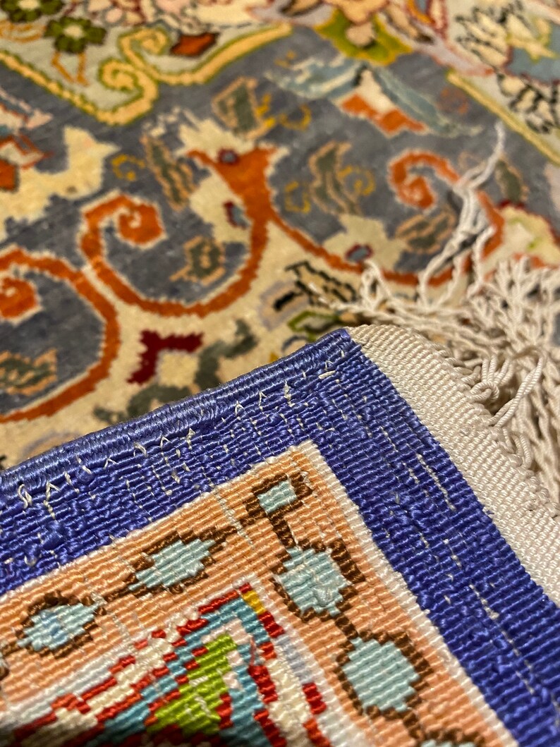 May include: Close-up of a blue and white rug with a detailed floral pattern. The rug has a fringe border and is woven with intricate details.