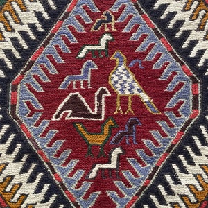 May include: A red, blue, and white patterned rug with a diamond-shaped design featuring stylized birds and animals. The rug has a traditional, folk art style.